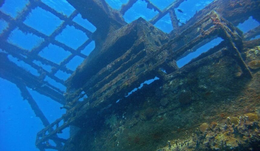 Encrusted metal wreckage of the Bajan Queen tug rising through clear blue water