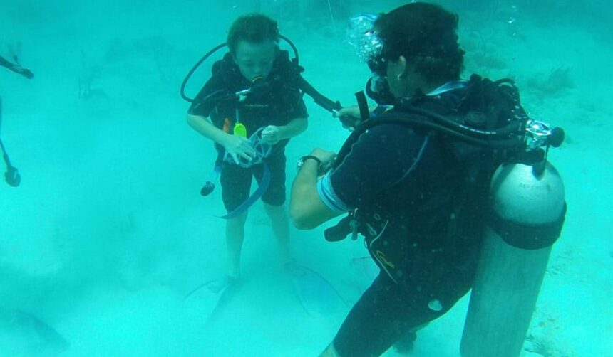 Instructor guiding a young diver over a sandy bottom in shallow, clear Barbados water