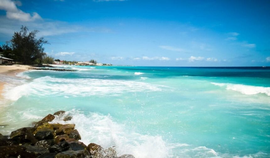 Turquoise surf breaking over dark rocks on a tree-lined Barbados beach
