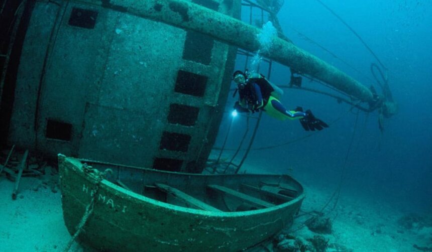 Diver with a dive light exploring the Hema I shipwreck in Grenada, a small boat upright on the sand