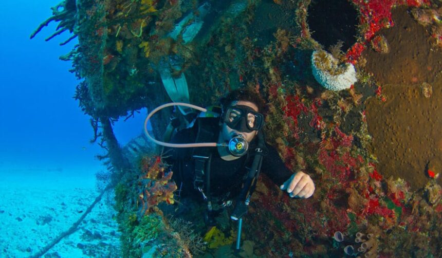 Scuba diver beside the coral-encrusted hull of the sunken fishing boat at Fish Highway