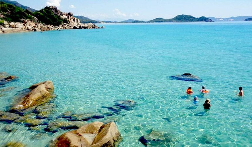 Clear turquoise shallows and granite boulders at Lobster Beach with swimmers wading offshore
