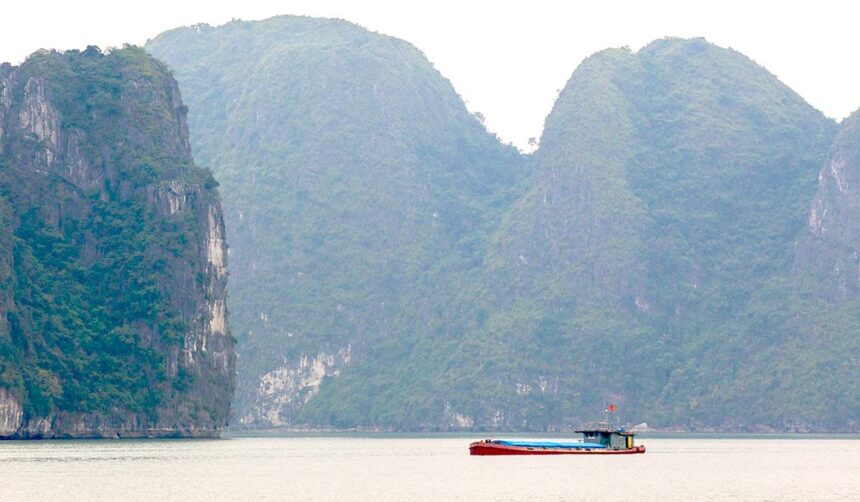 Forested limestone islands rising from calm water at Hon Ko with a small red cargo boat passing