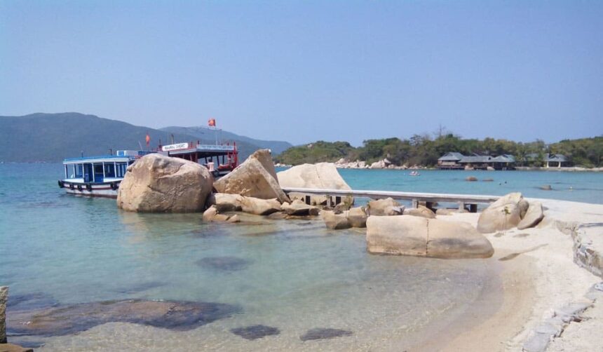 Dive boats moored beside pale boulders on a shallow turquoise beach in Vietnam