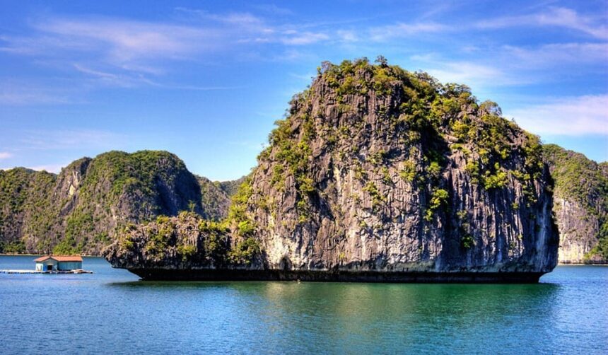 Steep limestone karst rising straight out of calm sea next to a small floating house