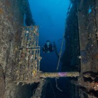Diver framed between rusted, encrusted sections inside the Dona Marilyn wreck