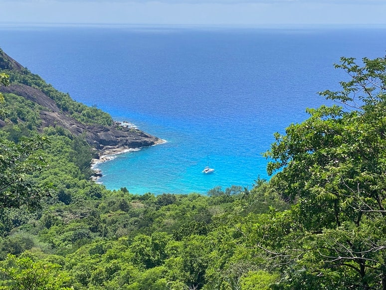 A catamaran anchors in a turquoise bay below green hills in the British Virgin Islands