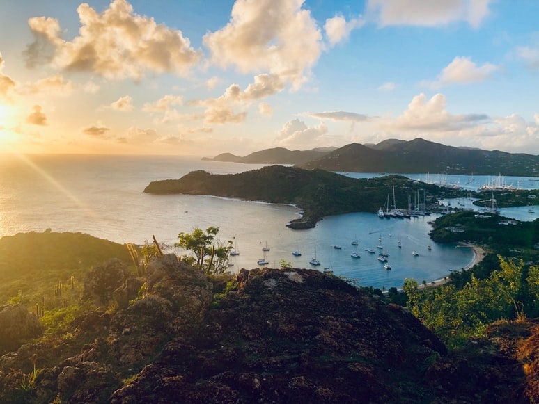 Sailboats fill a harbor below green hills at sunset in Antigua