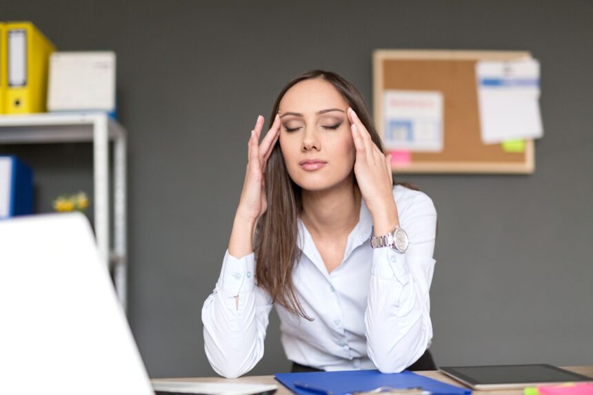Woman sitting at a desk pressing her fingers to her temples in stress
