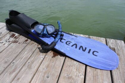 Blue Oceanic Predator fins with a mask and snorkel laid out on a wooden dock beside green water