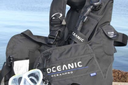 Black Oceanic OceanPro BCD with inflator hose beside a yellow mask at the water's edge