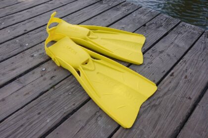 Pair of yellow Oceanic Accel open heel fins resting on weathered dock planks