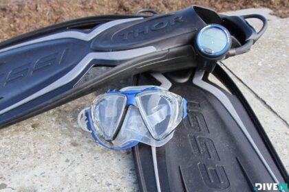 Cressi Penta+ mask propped on black Cressi Thor fins next to a round dive gauge