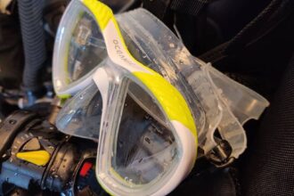 Wet Oceanic Discovery mask with yellow and white trim resting on a BCD and regulator after a dive