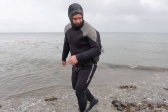 DIVEIN tester walking out of the sea in the hooded Northern Diver 7mm rear entry semi dry wetsuit