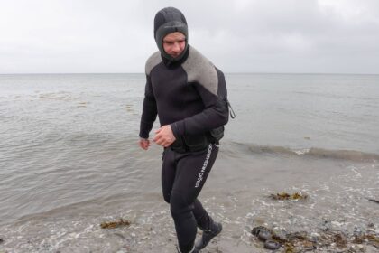 DIVEIN tester walking out of the sea in the hooded Northern Diver 7mm rear entry semi dry wetsuit