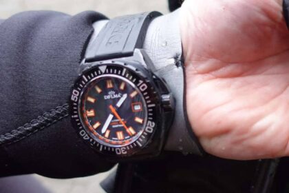 Delma Shell Star Black Tag dive watch with orange markers worn over a black wetsuit sleeve