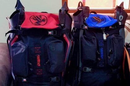 Two packed AKONA Globetrotter dive bags in red and blue with fins strapped to the tops