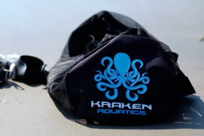 Kraken Aquatics mesh dive bag lying on wet sand beside a dive mask