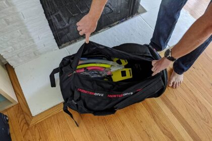 Our tester loading a snorkel and dive gear into the black Meister Dive mesh duffel on a hardwood floor