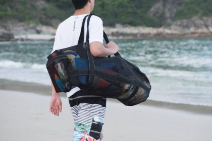 Person carrying a loaded Bulex XXL mesh dive duffel over one shoulder while walking on a beach