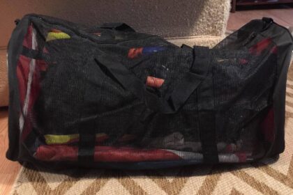 Black Scuba Max mesh duffel packed full of dive gear and resting on a rug indoors