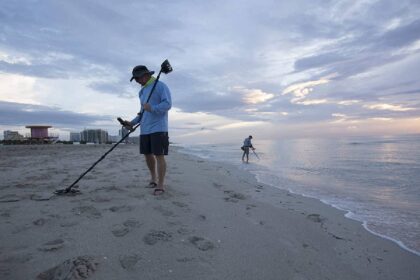 Detectorist sweeping the sand at dawn while a second searches the shallows further down the beach