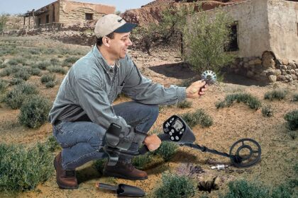Detectorist kneeling on dry scrubland, inspecting a coin found with a Bounty Hunter metal detector