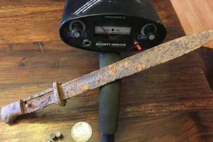Bounty Hunter Tracker IV control box on a wooden table with a rusted blade, an old coin and shell casings