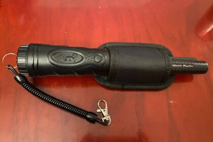 Handheld waterproof pinpointer detector with its belt holster, coiled lanyard and clip on a wooden table