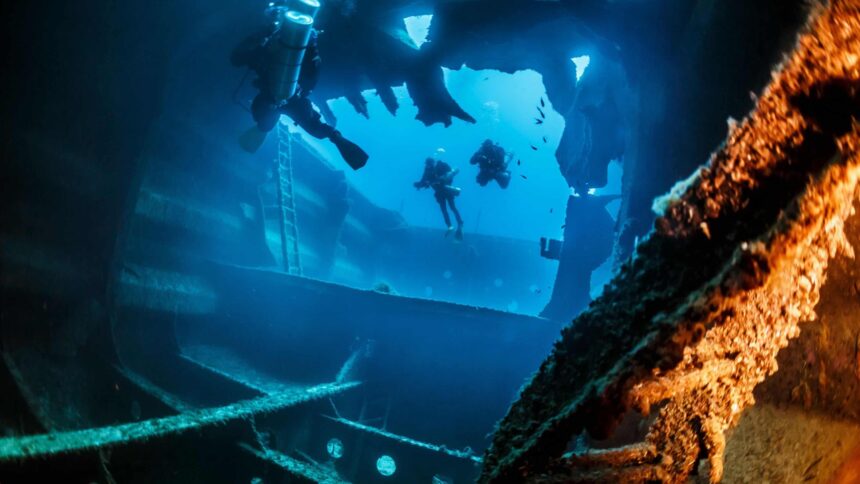 El Aguila Wreck Dive in Roatan Divers exploring the broken hull of the El Aguila wreck in Roatan