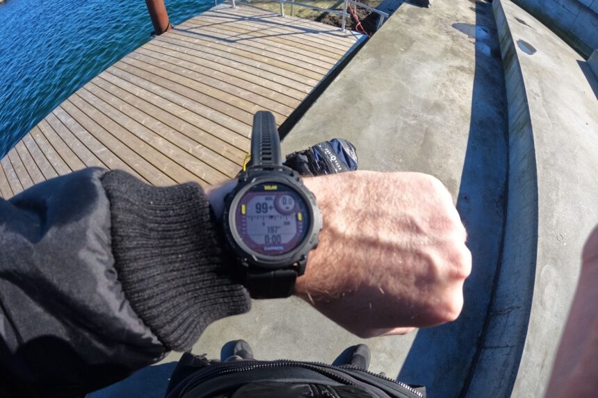 Our tester checking the Garmin Descent G1 Solar on the wrist on a wooden dock beside the sea
