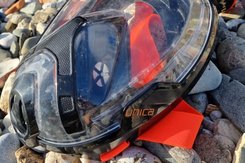 SEAC Unica Mask Lens And Branding Close-Up Close-up of the SEAC Unica full face mask resting on pebbles, Unica branding and clear lens in view