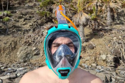 Our tester wearing the teal Ocean Reef Aria QR+ full face snorkel mask on a rocky shore