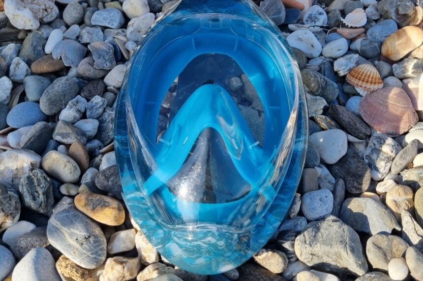 Subea Easybreath 500 lying lens up on pebbles with the blue inner nose pocket seen through the lens
