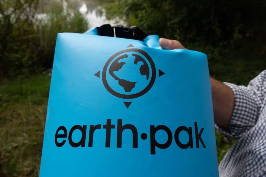 Close-up of the Earth Pak logo on the blue roll-top dry bag held up beside a lake