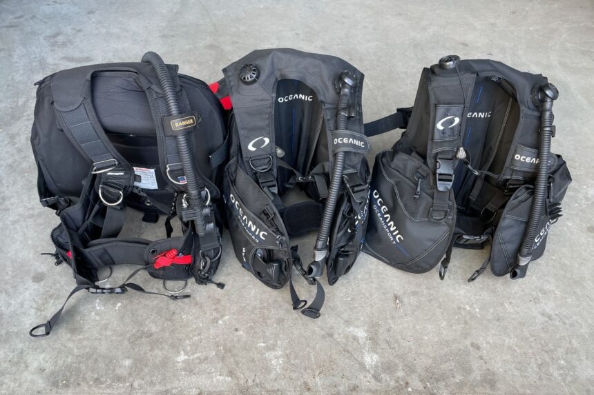 Oceansport Lined Up With Other BCDs Several black BCDs lined up side by side on a concrete floor, with Oceanic Oceansport jackets among them