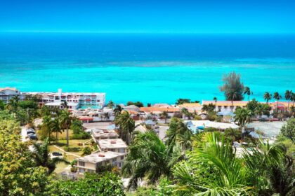Jamaican coastal town with palms and low buildings above a bright turquoise reef shelf