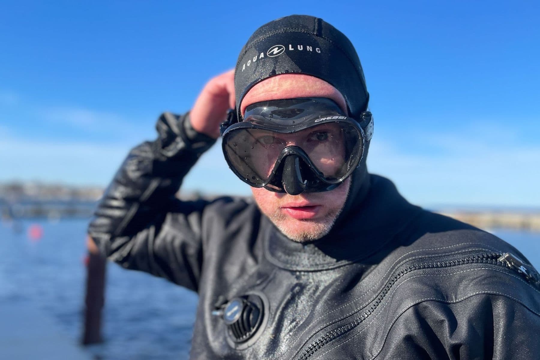 Our tester lifting the Cressi F1 onto his hooded head in bright sun beside the water