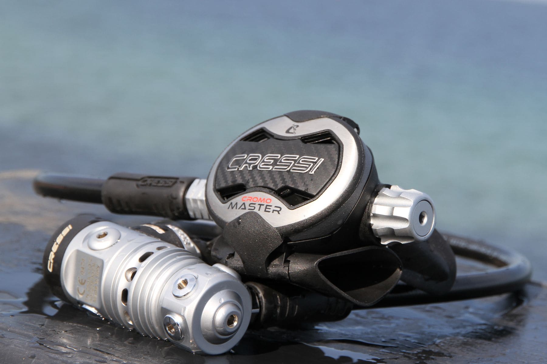Cressi Cromo Master regulator first and second stage resting on a wet surface with the sea behind it