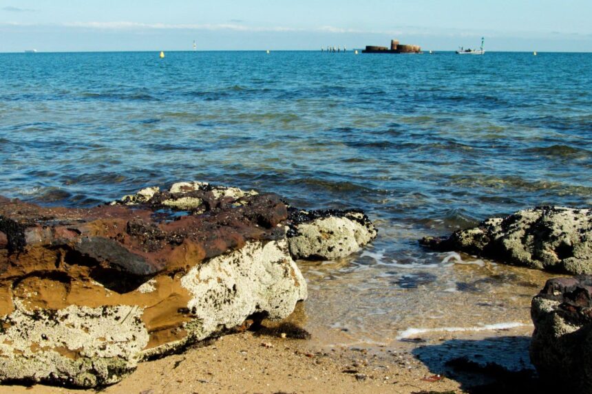 Rocky shoreline with shallow clear water and a wreck breaking the surface out on the horizon