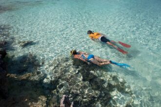 Two snorkelers finning over a shallow coral reef in clear turquoise water