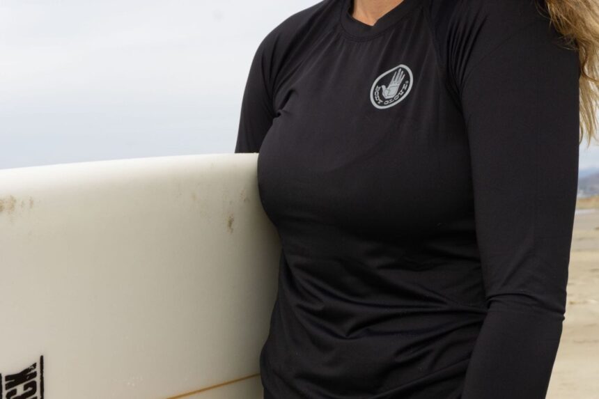 Our tester in a black long-sleeved Body Glove rash guard carrying a surfboard on the beach
