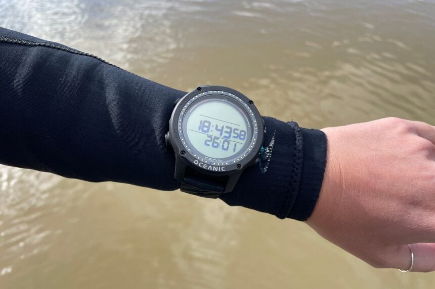 Oceanic Geo Air Worn On The Wrist Our tester wearing the Oceanic Geo Air over a wetsuit sleeve beside murky brown water