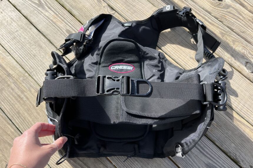 Our tester holding the Cressi Travelight BCD by its cummerbund on a dock, showing the chest strap and buckle