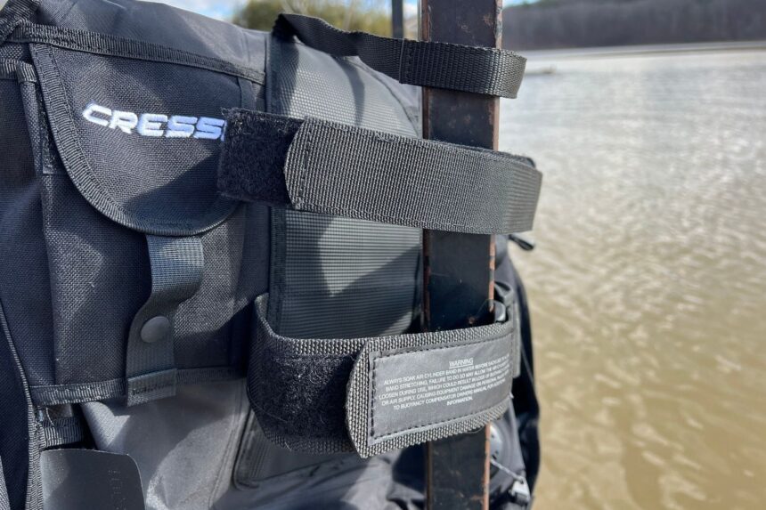 Close-up of the Cressi Travelight BCD tank band and safety strap fastened around a dock post by the water