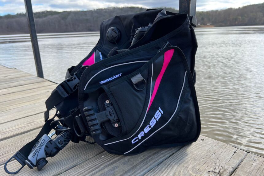 Cressi Travelight BCD standing on a lakeside dock with its inflator hose and slide-through buckle visible