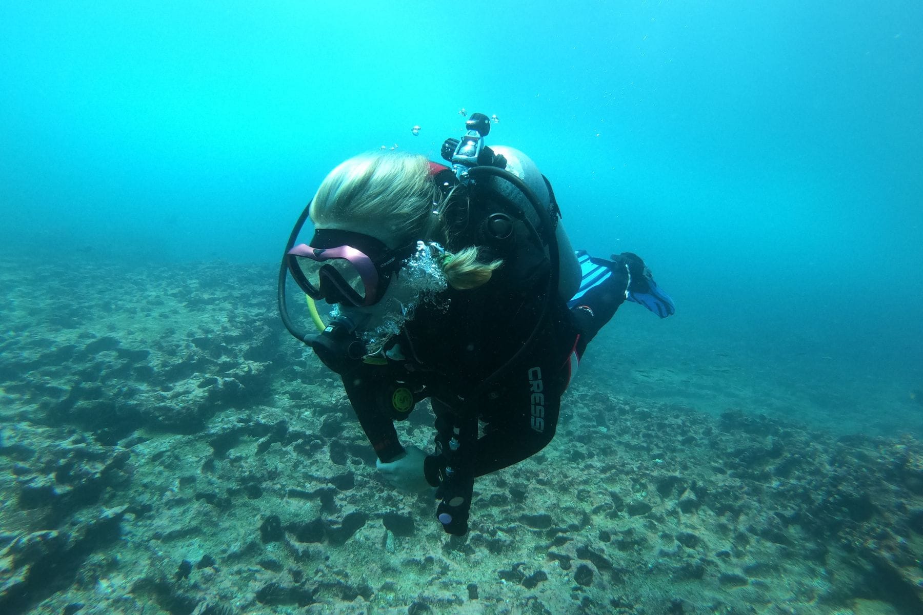 Our tester diving over a rocky reef wearing the Cressi A1 mask, with a camera on the tank