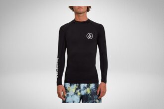 Man in a black Volcom long sleeve rash guard with circle stone logo and printed boardshorts