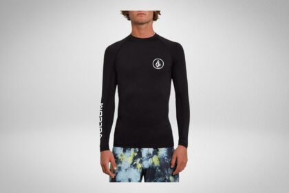Man in a black Volcom long sleeve rash guard with circle stone logo and printed boardshorts